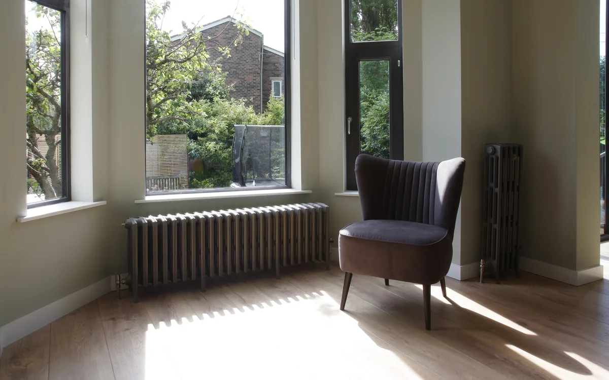 Cast iron column radiators under a bay window in a sunlit living room
